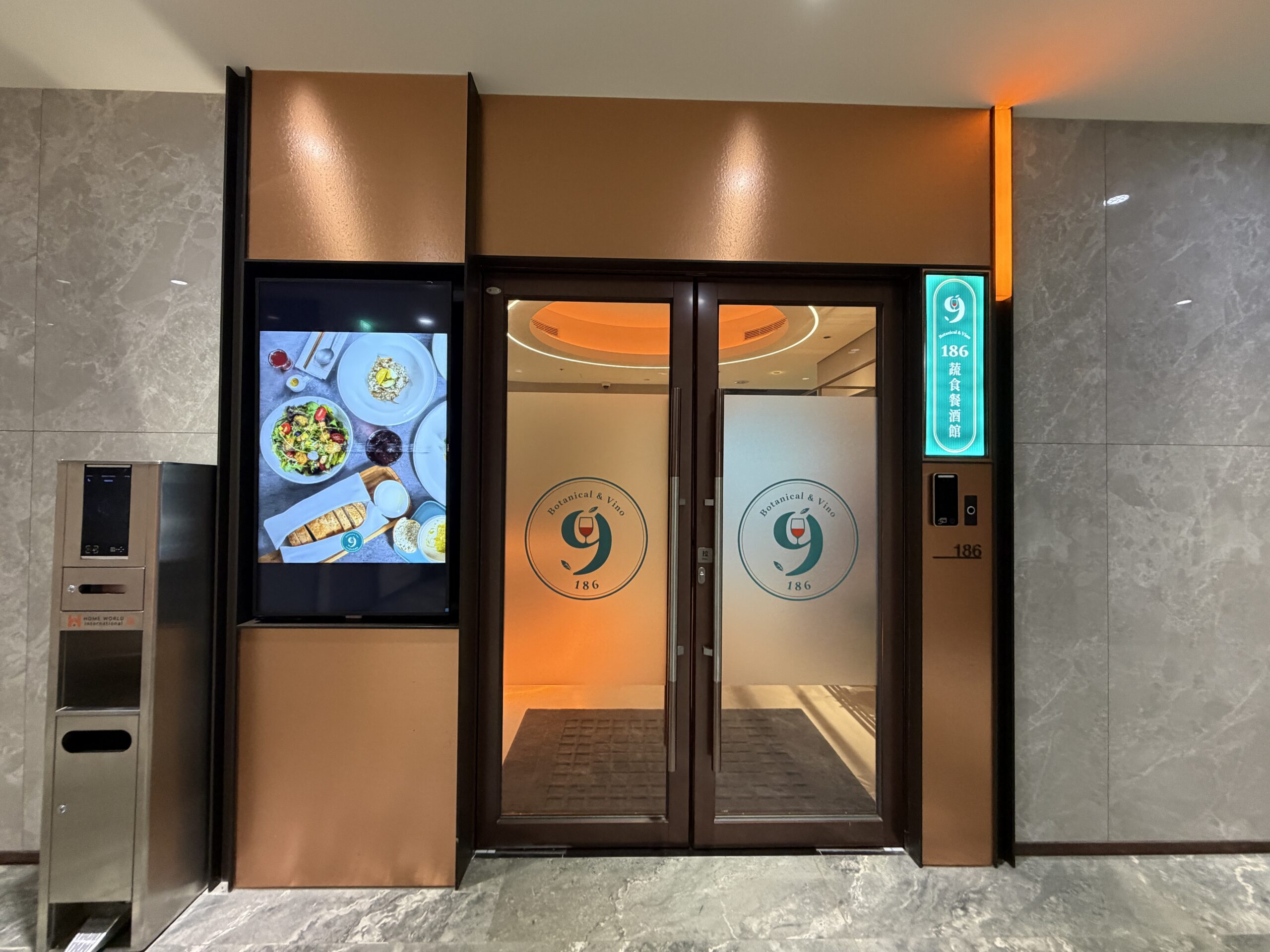 餐廳大門，雙玻璃門印著Botanical & Vino與186蔬食餐酒館字樣，一旁掛著菜色照片電子看板