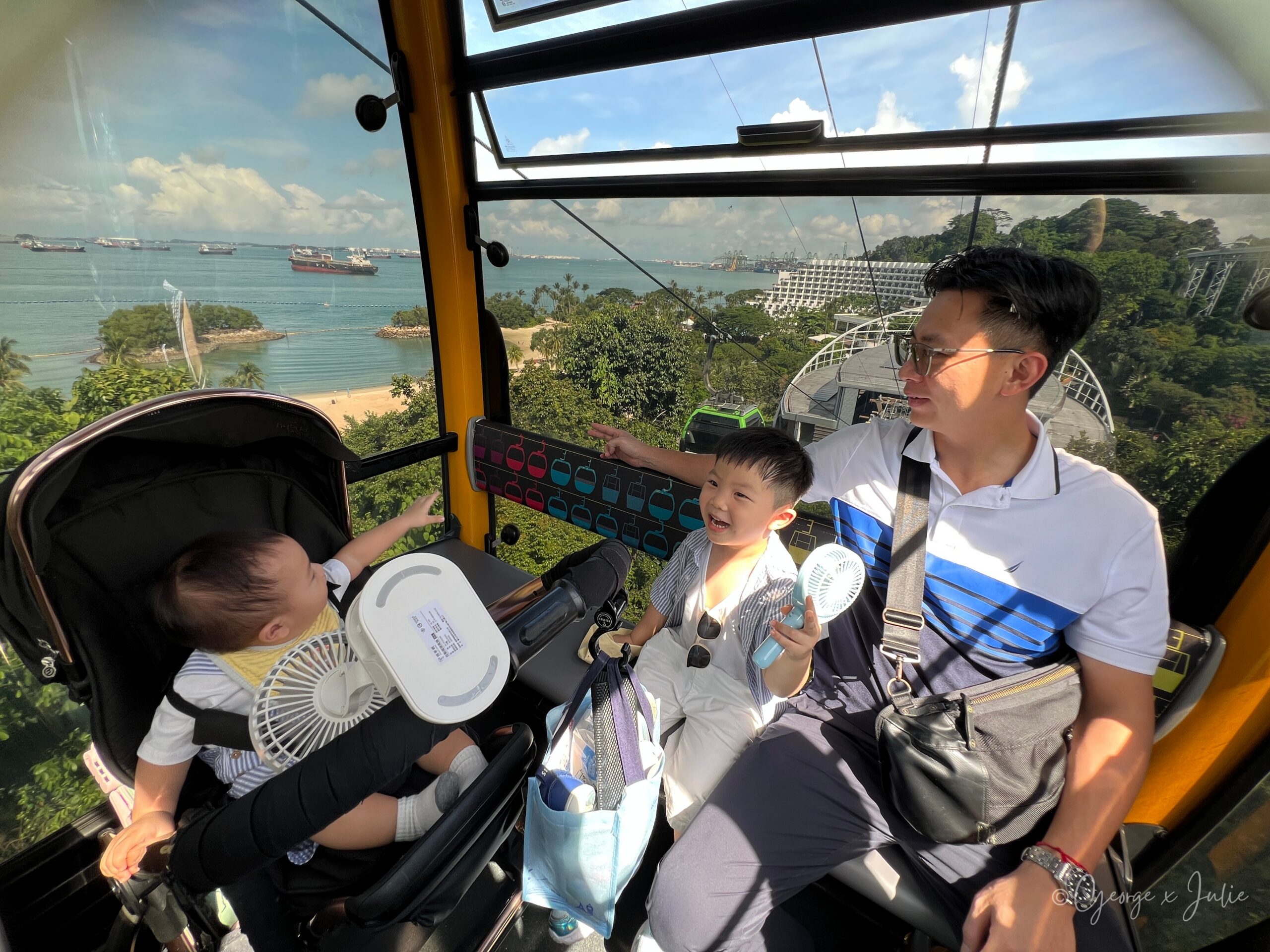 爸爸帶著兩個孩子站在車廂裡，窗外就是整片 Siloso 的海