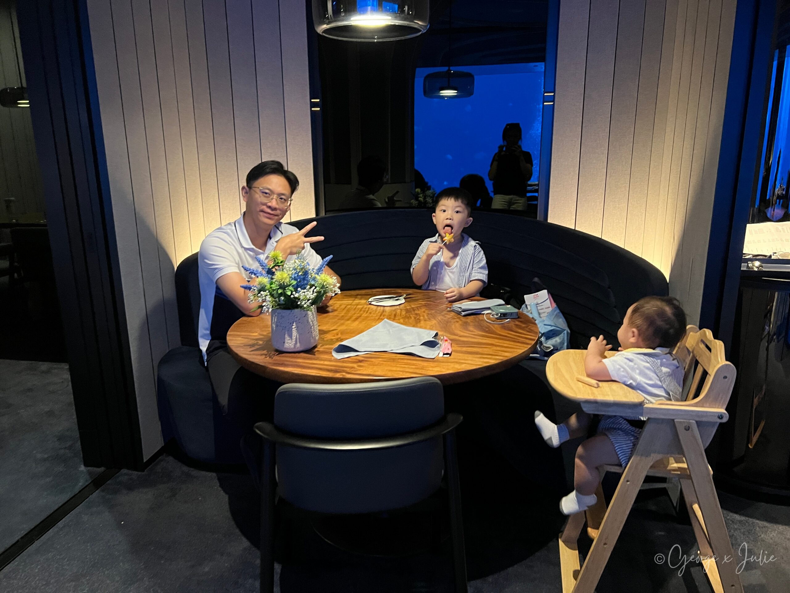 George和兩個孩子入座圓桌，桌上擺著花束，背景是水族箱