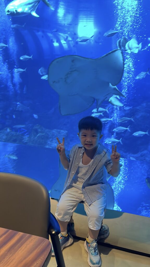 兒子比YA拍照，一隻魟魚剛好貼在他頭頂上方游過，畫面很有趣