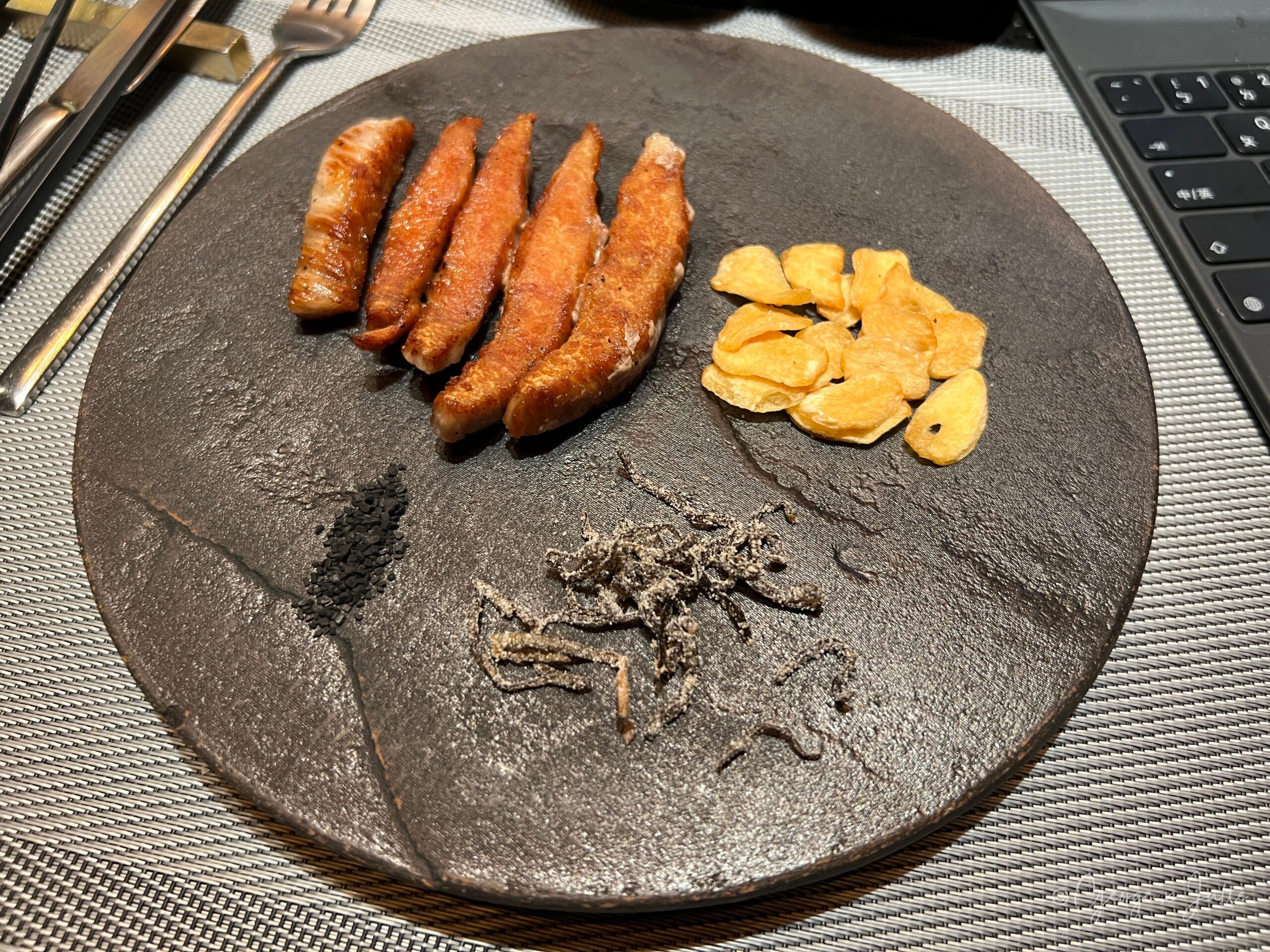松阪豬切條擺盤，配蒜片、夏威夷黑鹽與昆布
