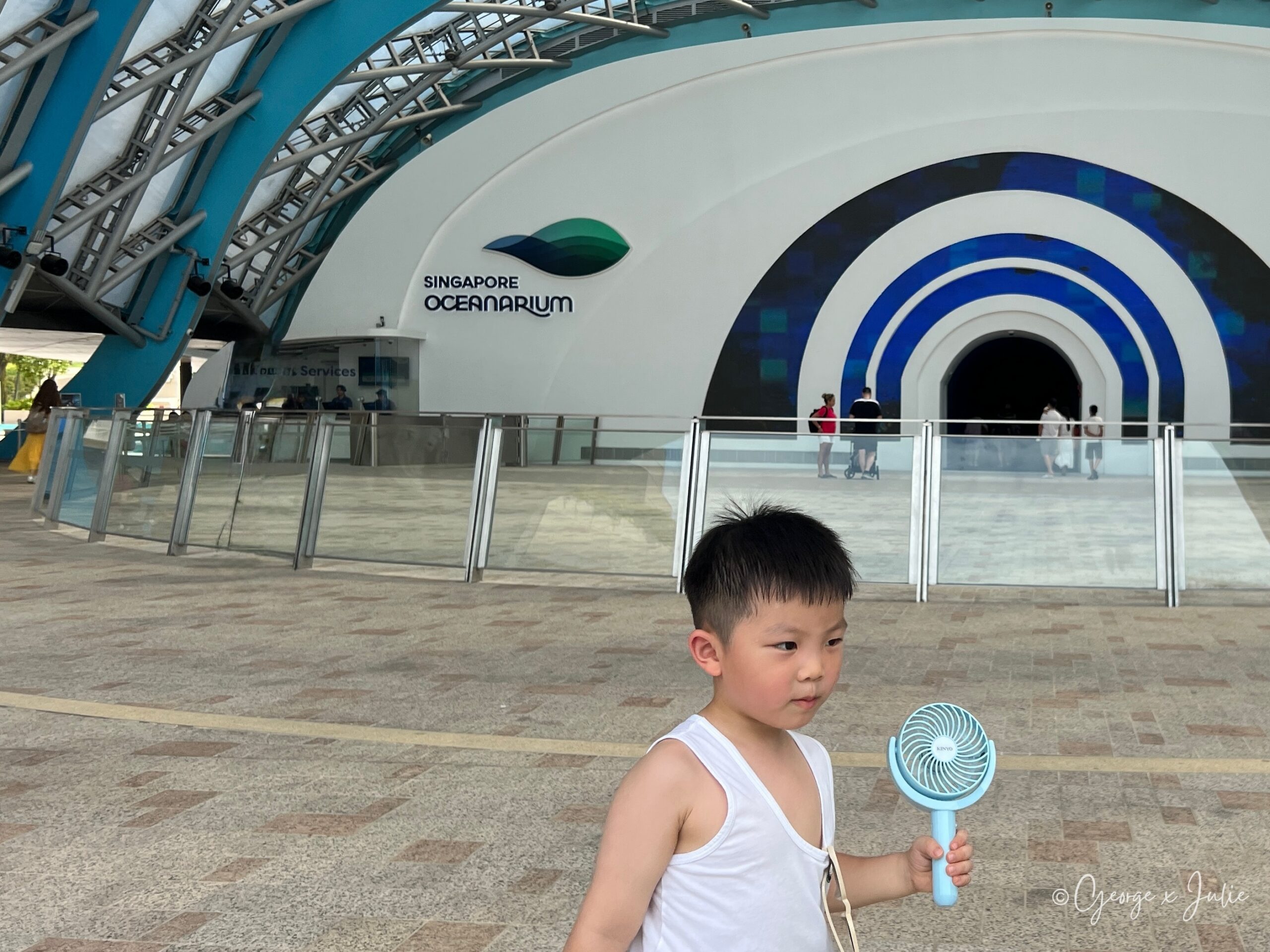 Jensen站在Singapore Oceanarium招牌前，手裡的小電風扇還沒放下