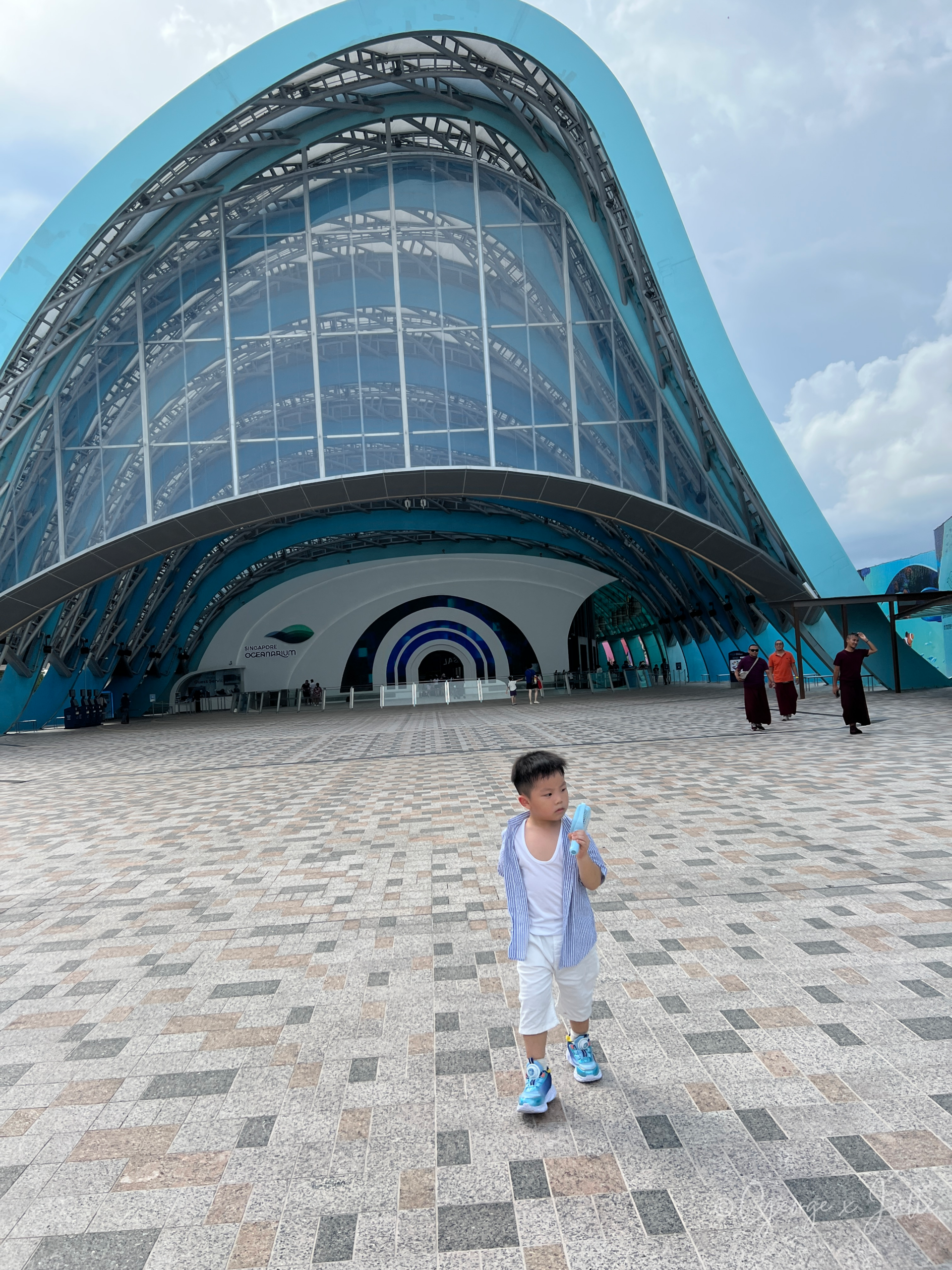 Jensen走在海洋館建築前，手裡拿著小電風扇，天氣熱到隨身電風扇沒離過手