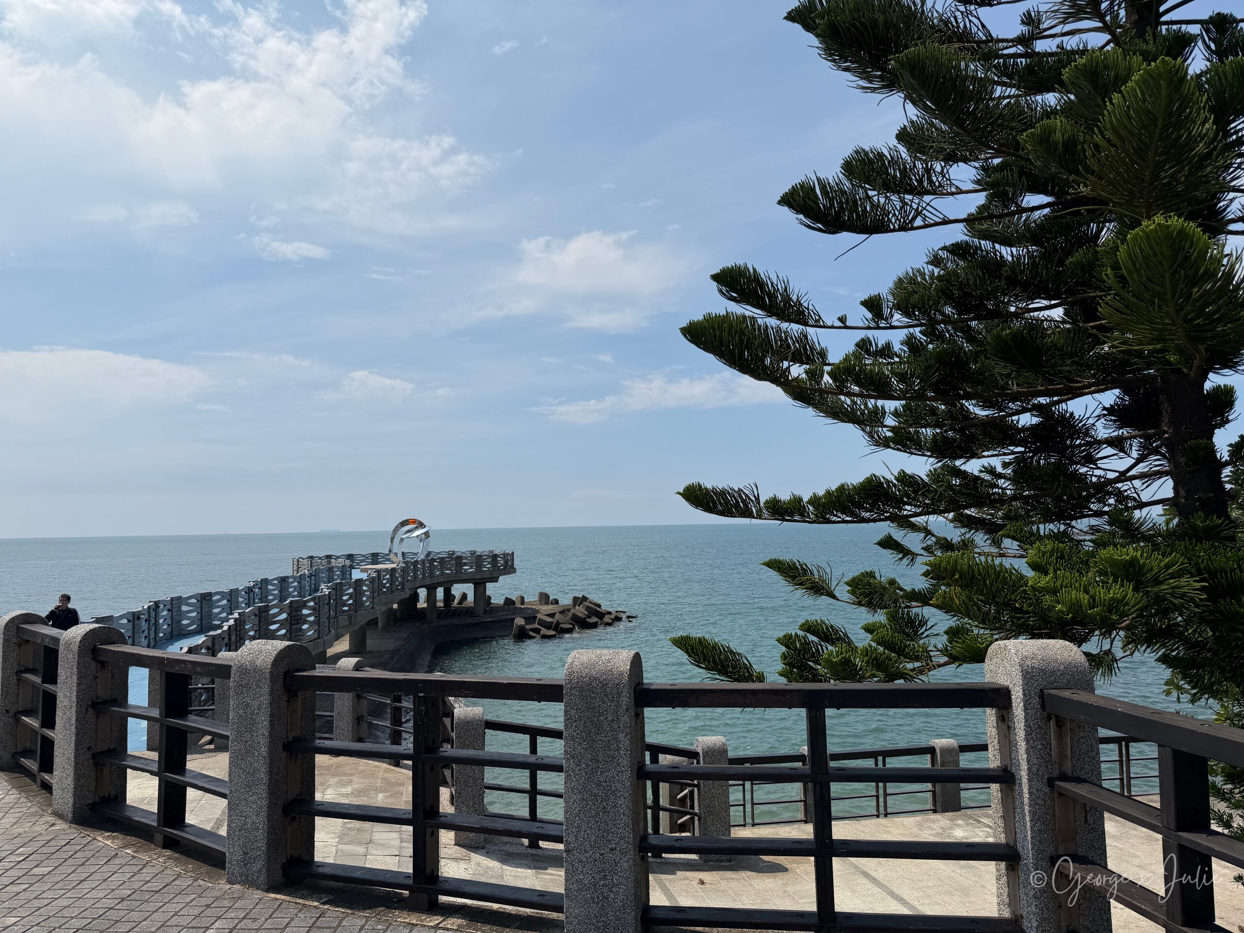 【新北三芝景點】芝蘭公園海上觀景平台|北海岸婚戒打卡海上步道 3 透過石柱欄杆與松樹枝葉,遠方可見延伸進海的觀景平台與裝置藝術