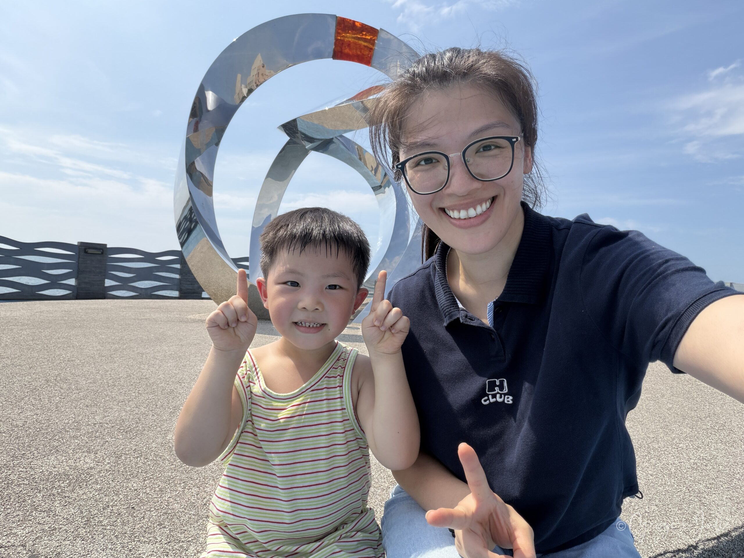 【新北三芝景點】芝蘭公園海上觀景平台|北海岸婚戒打卡海上步道 9 Julie和Jensen在不鏽鋼婚戒裝置藝術前自拍合照,背景是藍天