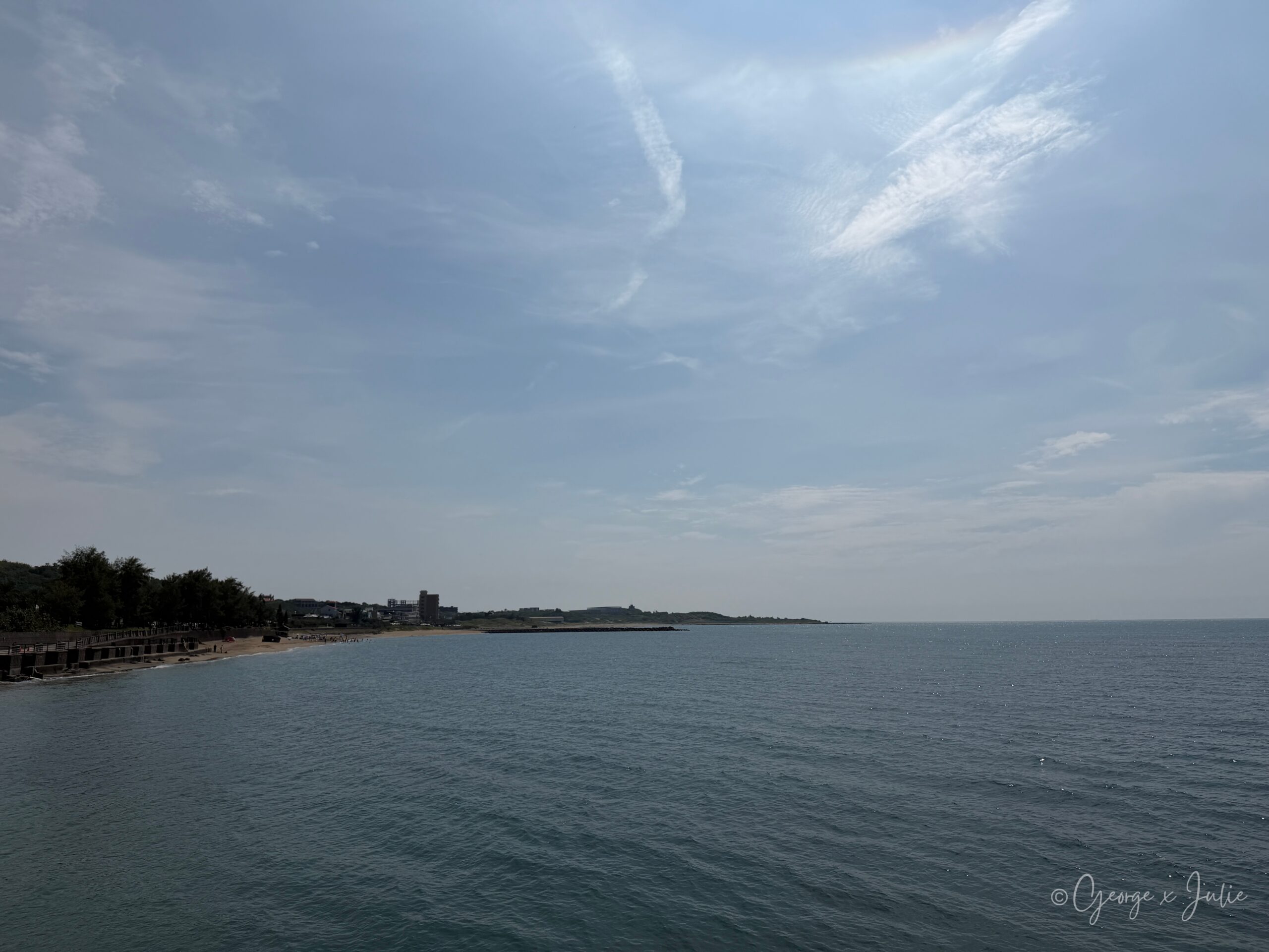 【新北三芝景點】芝蘭公園海上觀景平台|北海岸婚戒打卡海上步道 13 三芝海岸線全景,沙灘與遠方建築群,海堤步道延伸至畫面右側