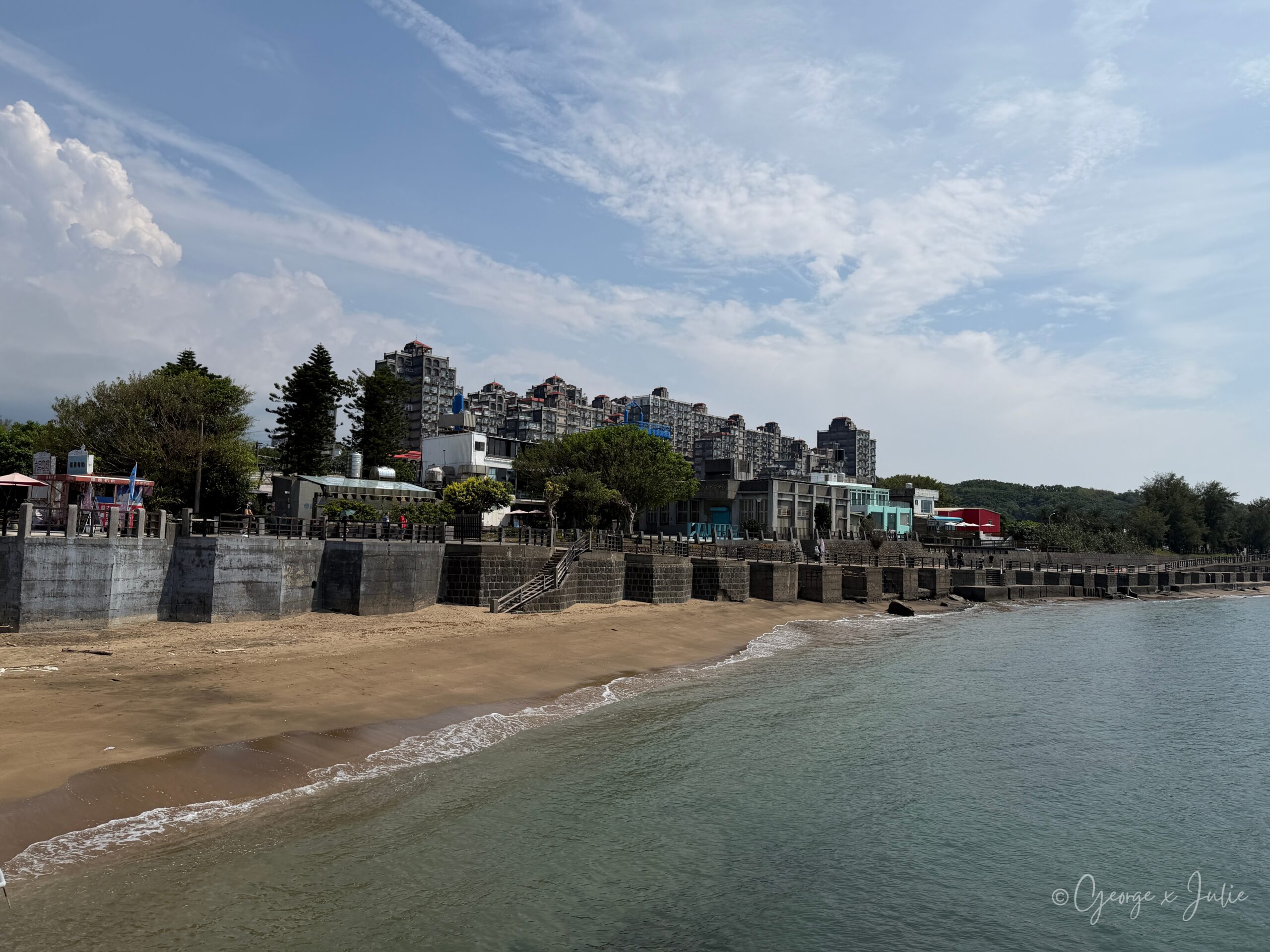 【新北三芝景點】芝蘭公園海上觀景平台|北海岸婚戒打卡海上步道 14 三芝沙灘與海堤,海堤中間有樓梯通往沙灘,遠方是樓房