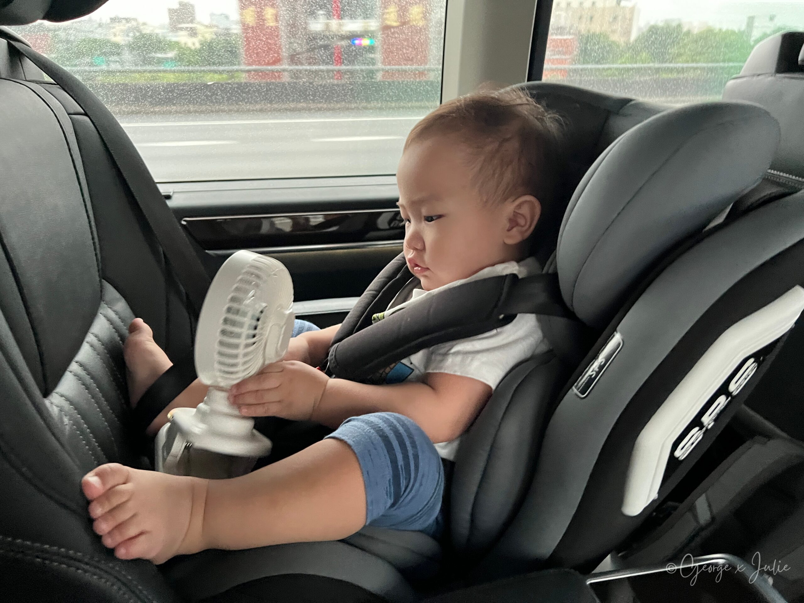 從家裡前往機場的車上，Morris 坐在汽座裡抱著小風扇