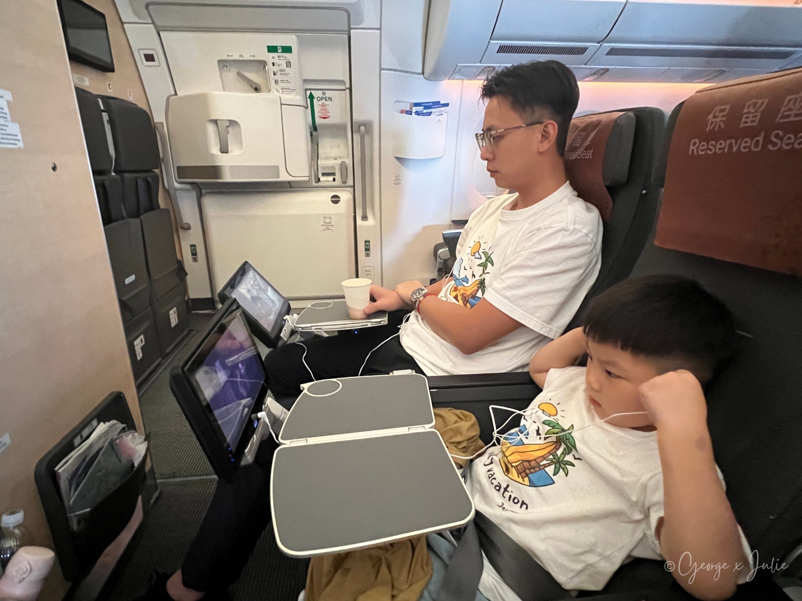 靠近艙門的座位空間，Jensen 使用座位螢幕，George 坐在旁邊陪他