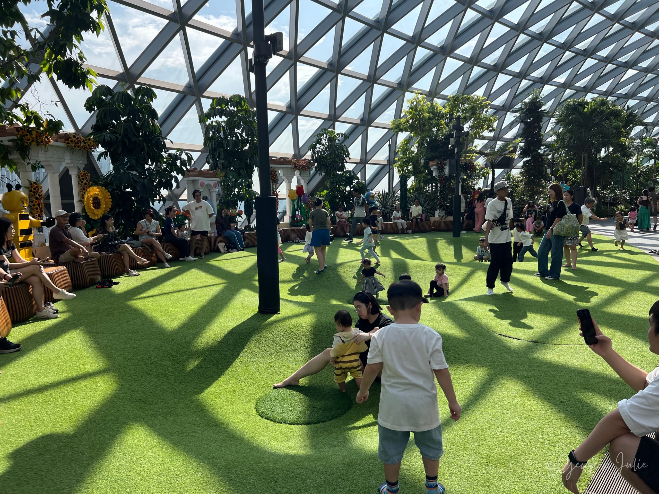 【新加坡親子景點】星耀樟宜星空花園Canopy Park|鏡子迷宮、天懸橋親子實玩攻略 13 雲霧碗(Foggy Bowls)的草坪上,向日葵與樂高蜜蜂造景擺在一側,Jensen 站著、Morris 在草地上爬行,Julie 在旁邊扶著