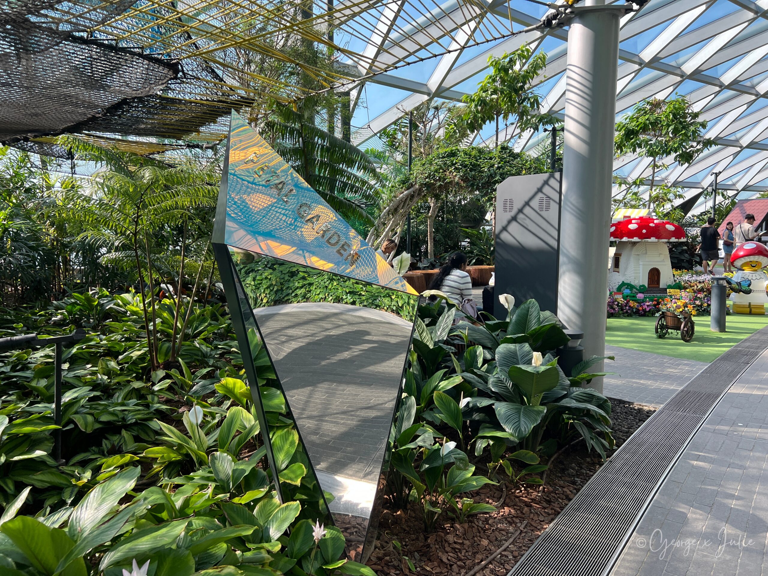 【新加坡親子景點】星耀樟宜星空花園Canopy Park|鏡子迷宮、天懸橋親子實玩攻略 10 PETAL GARDEN(花卉園)幾何鏡面招牌立在步道旁,背景可以看到樂高蘑菇屋