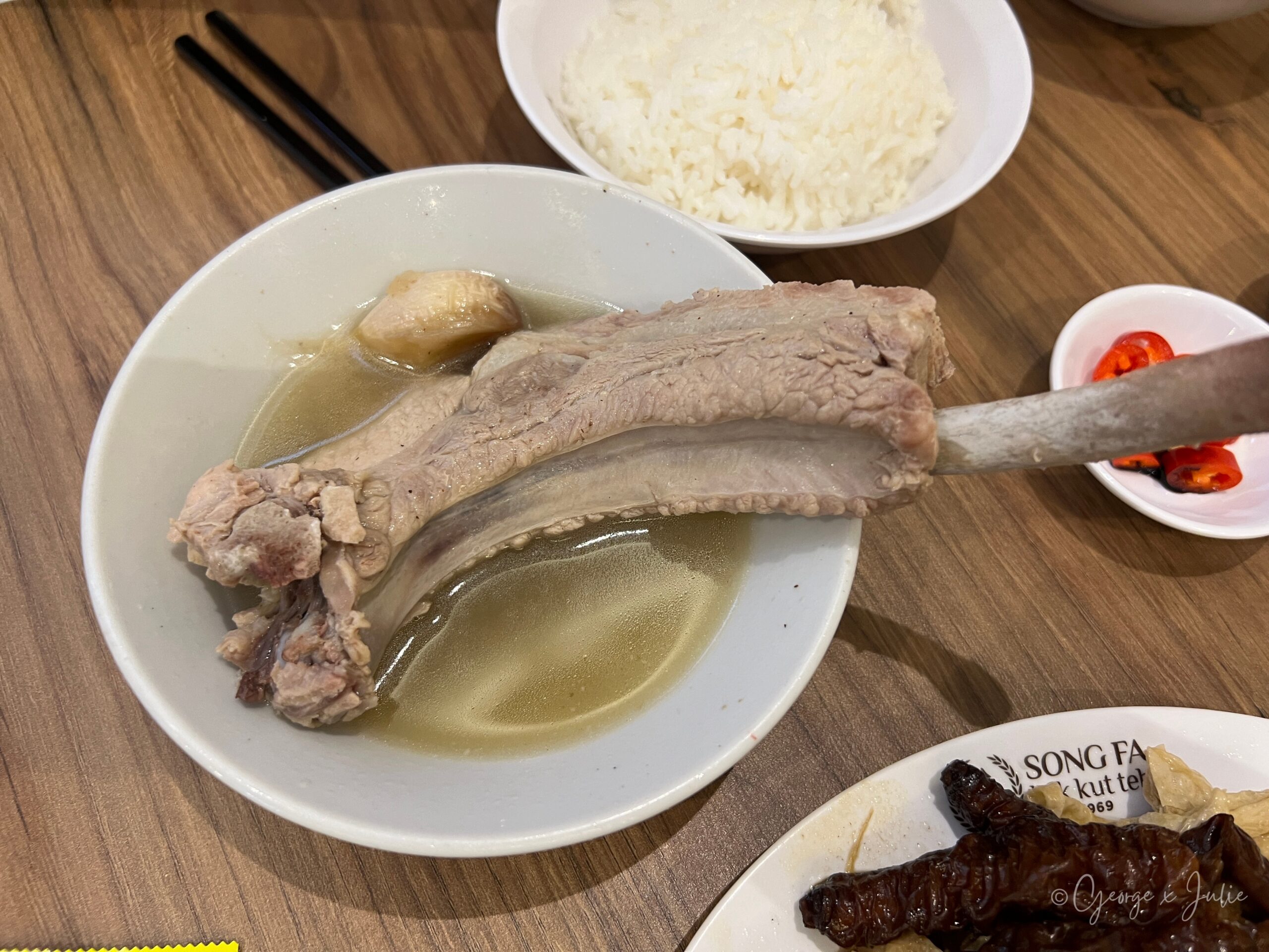 松發肉骨茶特級龍骨湯，大支龍骨泡在胡椒清湯裡，一旁配白飯與辣椒沾醬