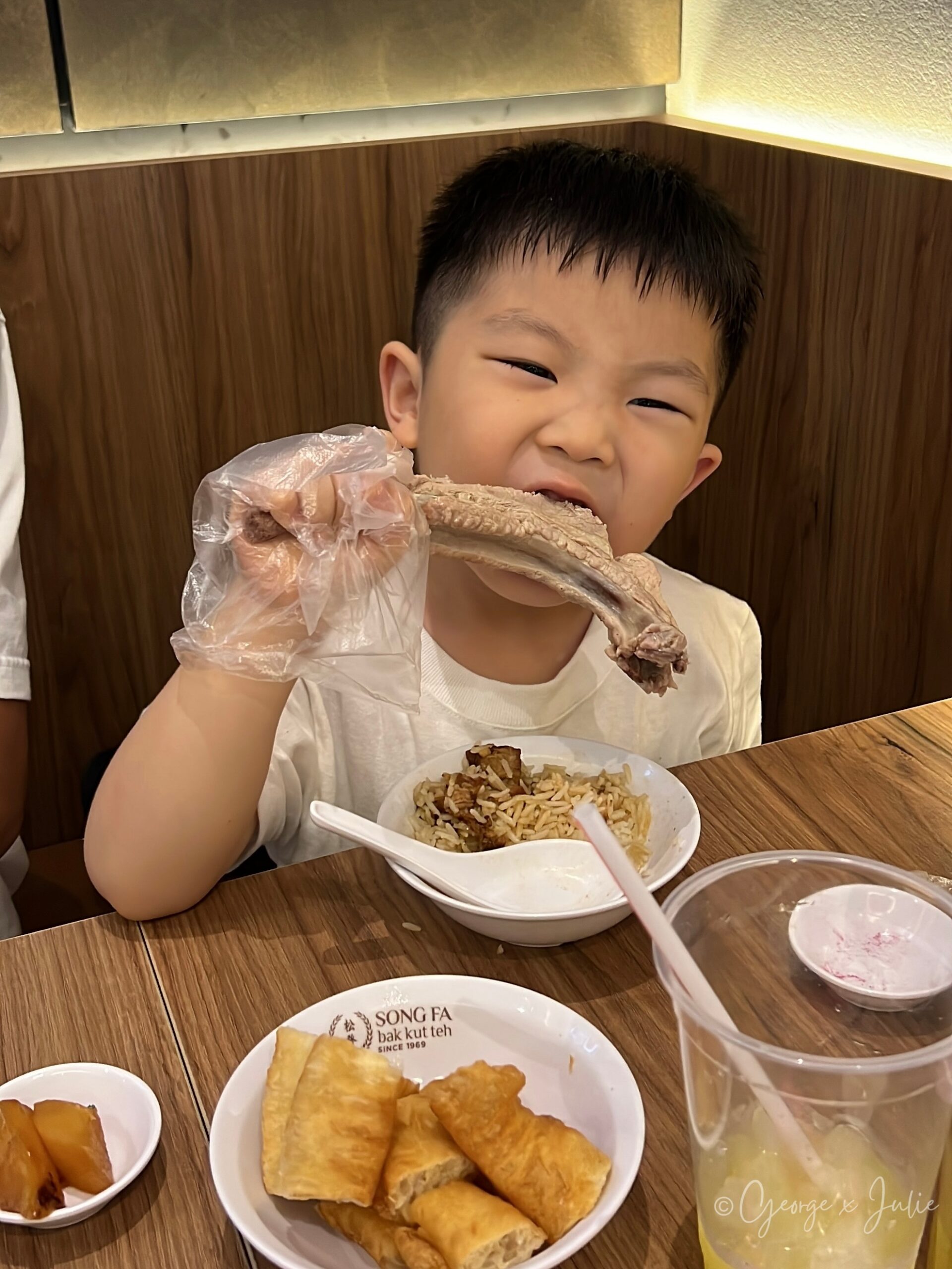 松發肉骨茶用餐，Jensen戴著塑膠手套啃排骨骨頭，做鬼臉，桌上還有油條與酸柑水