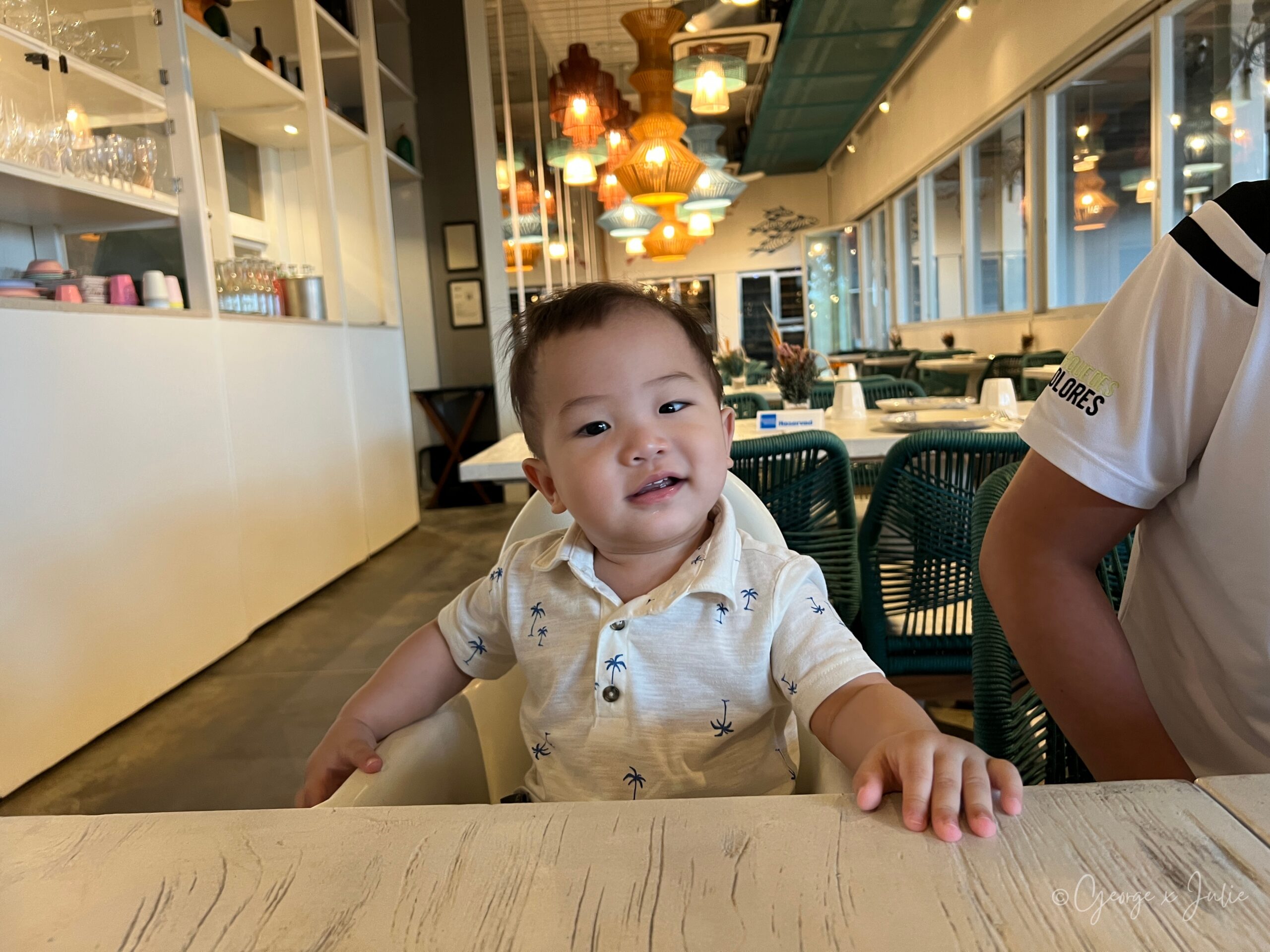 【新加坡美食】FOC by the Beach|聖淘沙Tanjong Beach泳池畔西班牙料理,親子海灘度假餐廳推薦 19 Morris坐在兒童椅上,手拿一片麵包,穿白色棕櫚樹印花polo衫