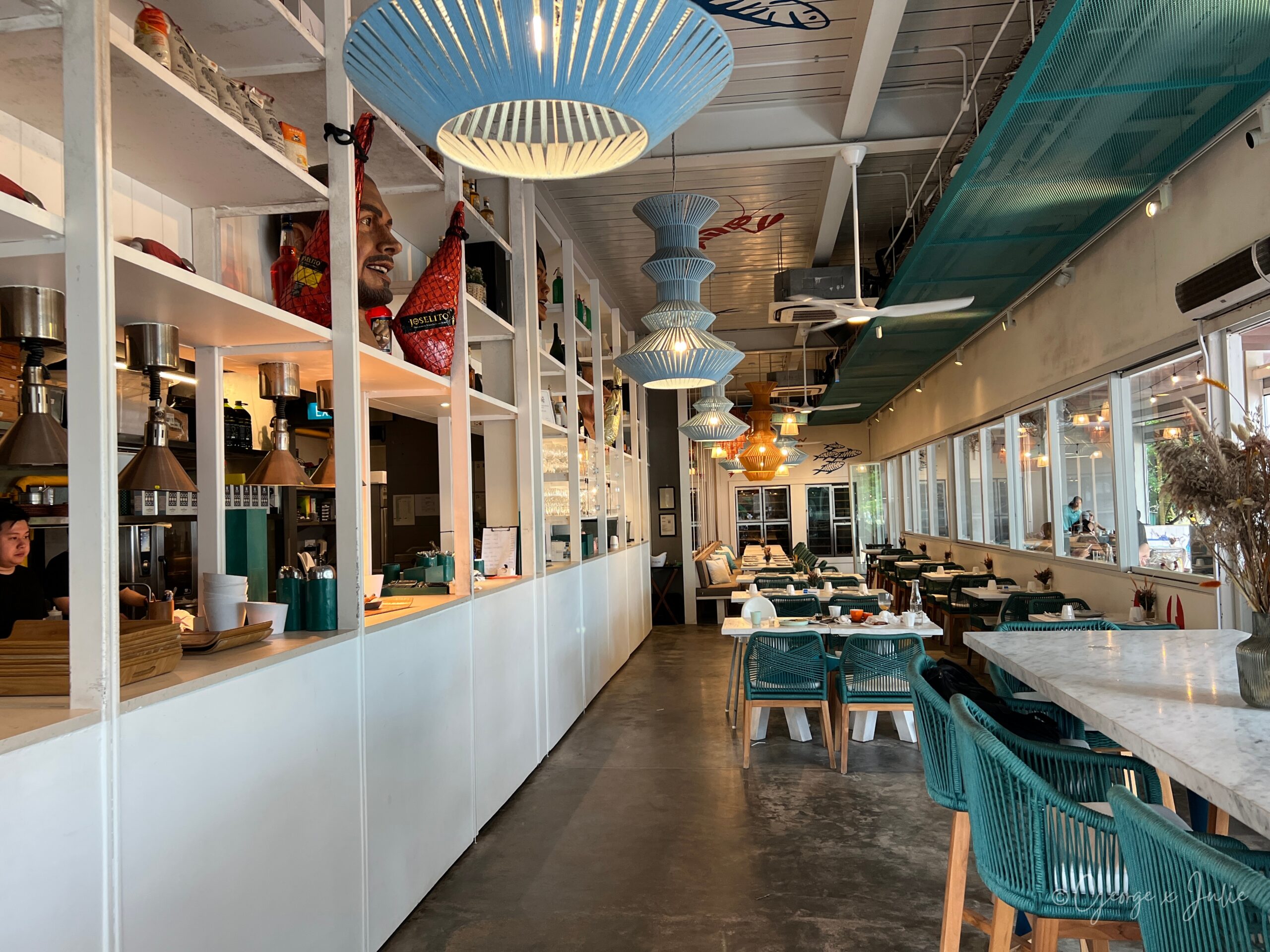 【新加坡美食】FOC by the Beach|聖淘沙Tanjong Beach泳池畔西班牙料理,親子海灘度假餐廳推薦 2 從吧檯望向用餐區的縱深視角,整排彩色編織吊燈與遠處落地窗