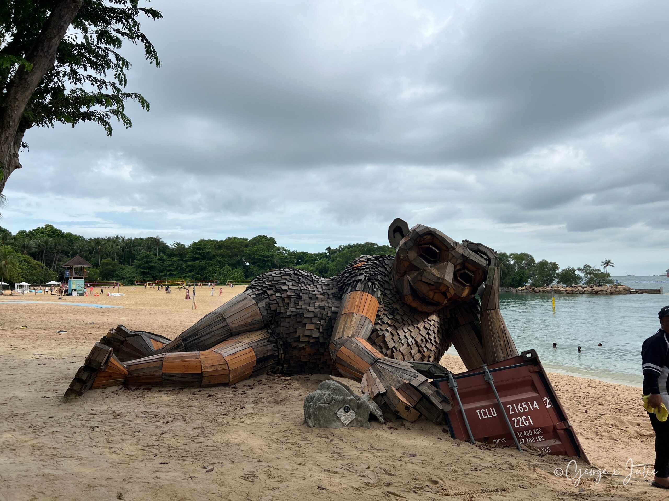 【新加坡景點】聖淘沙亞洲大陸最南端|Palawan Beach 90度椰子樹、吊橋免費踩點 5 沙灘上一隻用回收木料拼接而成的大型動物裝置藝術,倚著一只生鏽貨櫃造型裝置,後方是沙灘排球場
