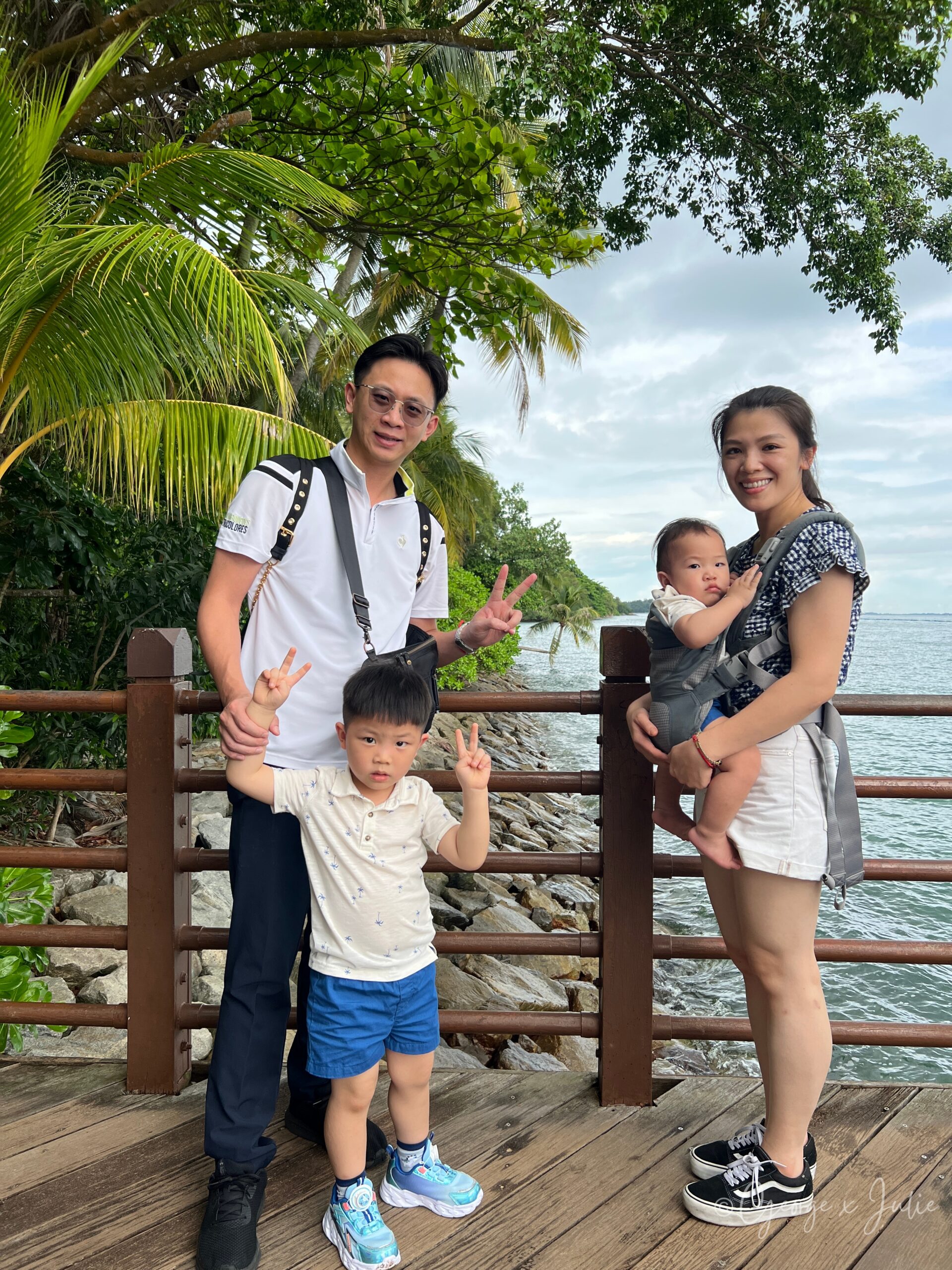 【新加坡景點】聖淘沙亞洲大陸最南端|Palawan Beach 90度椰子樹、吊橋免費踩點 13 全家人在木棧道欄杆前合照,George 牽著 Jensen,Julie 揹著 Morris,背景是海岸線
