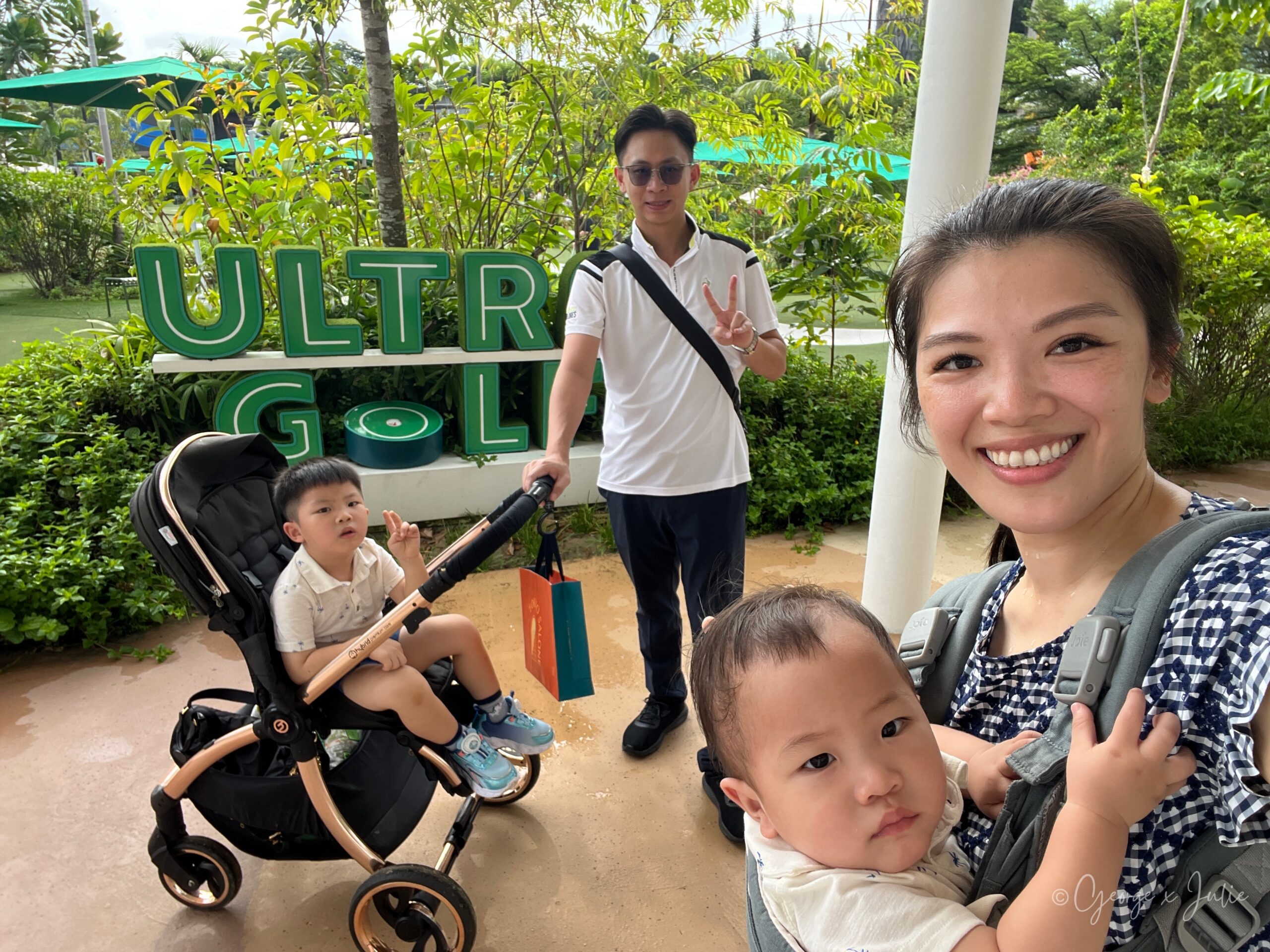 全家在 ULTRA GOLF 招牌前的自拍，Jensen坐在推車上、George站在後方比出勝利手勢，Morris在前面的背帶裡