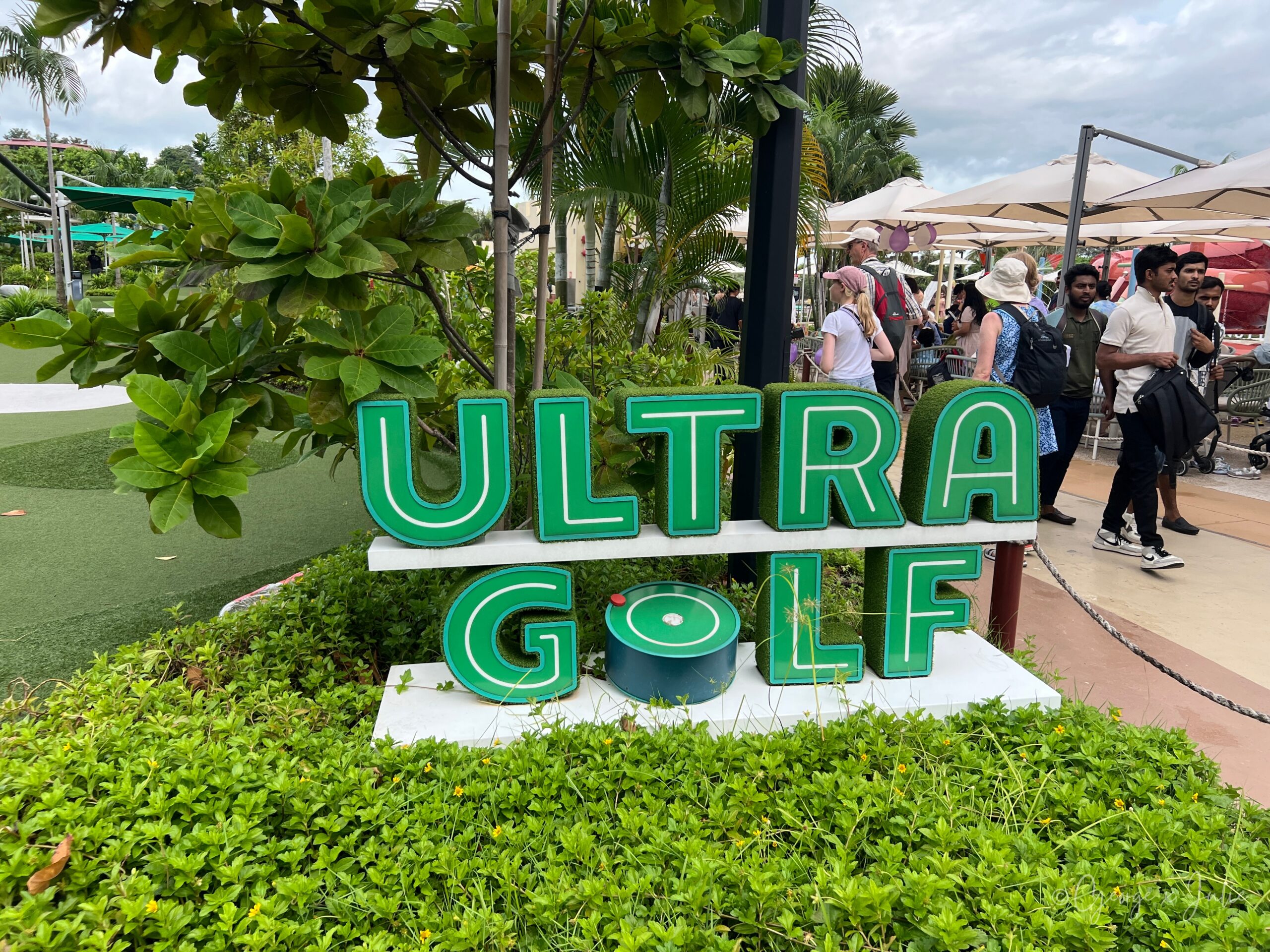 ULTRA GOLF 草皮字樣的招牌特寫，右邊是經過的遊客與園區的餐飲區